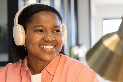 African american woman smiling, listening with wireless headphones at home desk workspace