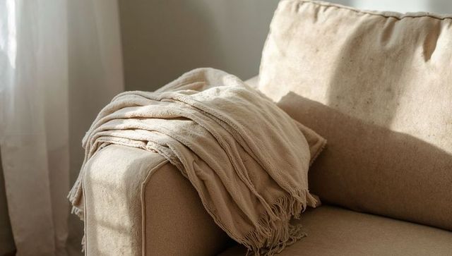 Beige throw draping over sofa arm with sheer curtain sunlight for cozy neutral decor
