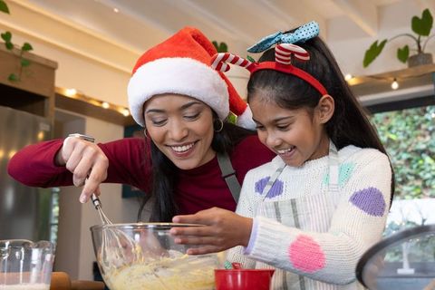 Asian mother and daughter baking holiday treats, whisking batter, santa hat and reindeer