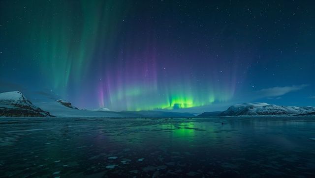 Vibrant aurora borealis illuminating snowy mountains and icy lake