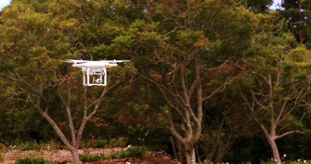 A drone equipped with a camera hovers in mid-air against a backdrop of lush green trees, capturing aerial footage. Drones like this are commonly used for photography, surveillance, and recreational purposes.