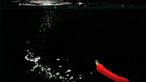 Red Chili Falling into Water with Bubbles in Slow Motion