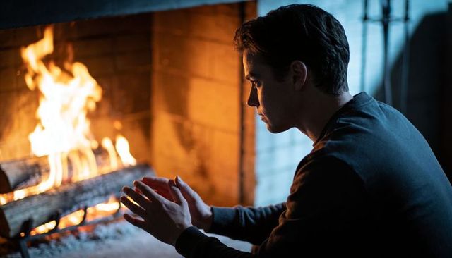 Man warming hands by fireplace in cozy cabin at night — contemplative hearthside moment