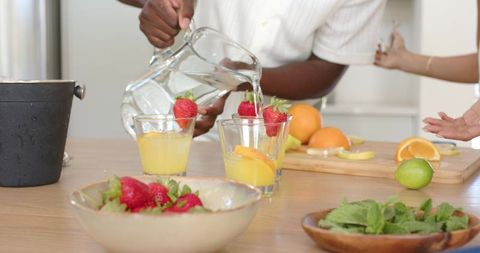 Pouring water into fruit-garnished glasses for fresh citrus drink preparation