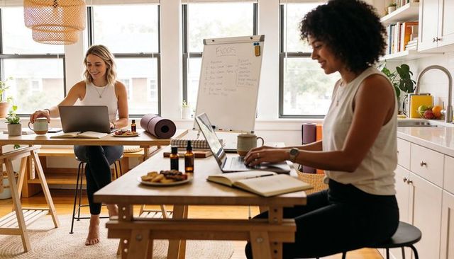 Sunlit home coworking women collaborating over laptops, notebooks and wellness bottles