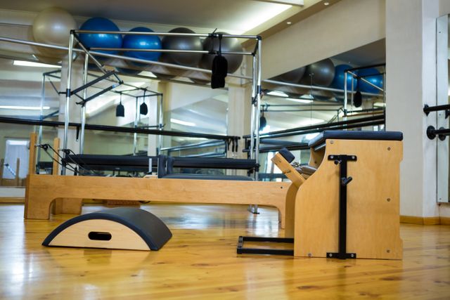 This image features a modern gym with various Pilates equipment arranged on a wooden floor. Ideal for use in fitness blogs, gym advertisements, wellness websites, and health-related articles to illustrate professional workout environments and promote healthy lifestyles.