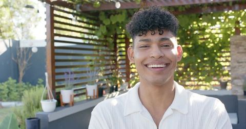 Smiling man standing under sunlit pergola wearing collared shirt, backyard lifestyle