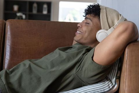 African american man relaxing on leather couch listening to music with white headphones