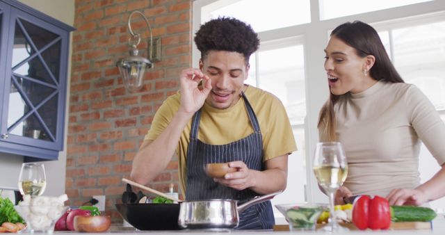 This engaging image of a happy biracial couple cooking and laughing in a modern kitchen is ideal for promoting family life, relationship quality, and home cooking. The photograph is perfect for use in lifestyle blogs, cooking websites, social media campaigns, advertisements for kitchen products, and home decor magazines. The warm and joyful atmosphere can attract audiences looking for authentic and heartwarming content related to love and togetherness.