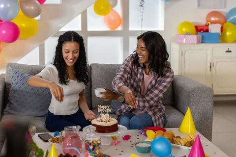 Mother and teen daughter adding sprinkles to birthday cake celebrating joyful home party