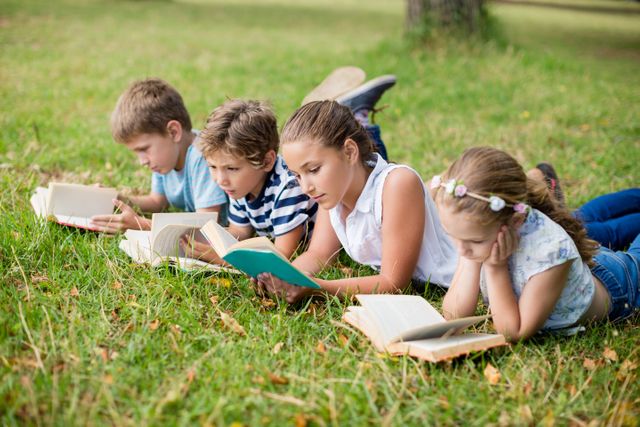 Children lying on grass in a park, engrossed in reading books. Ideal for educational content, promoting reading habits, outdoor activities, and childhood learning. Suitable for use in school brochures, library promotions, and summer camp advertisements.