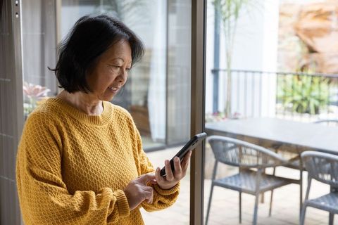 Senior woman in yellow sweater using smartphone by cozy patio