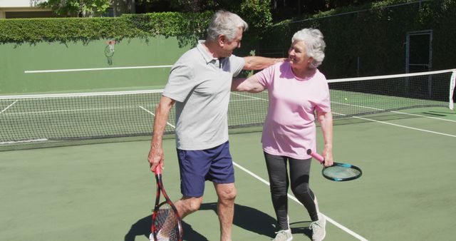Happy caucasian senior couple embracing on outdoor tennis court in sun after playing a game. active retirement lifestyle sports hobby.