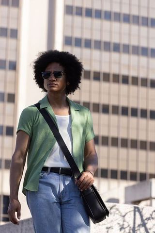 African american man walking downtown wearing sunglasses, crossbody bag, casual streetwear