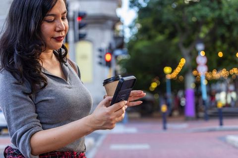 Urban twilight commuter checking smartphone while balancing coffee at busy crosswalk