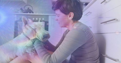 Kneeling woman bonding with white terrier in cozy kitchen with dreamy lens flare