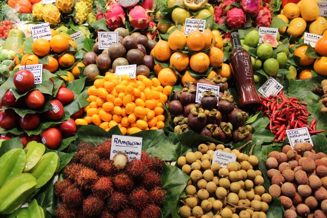 Colorful display of various exotic fruits arranged at market stall. The photo showcases vibrant colors and diverse shapes of different tropical fruits including rambutan, dragon fruit, longan, and more. This can be used in advertisements for food markets, healthy eating promotions, organic produce features, and articles about diverse diets.