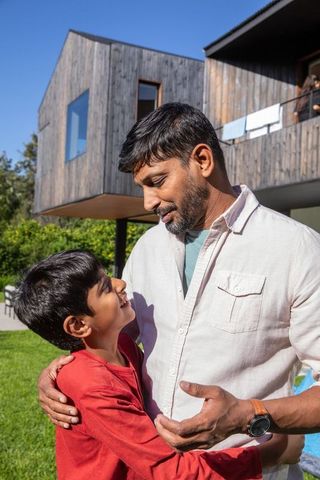 South Asian Father Bonding with Son Outdoors Near Modern Wooden Home