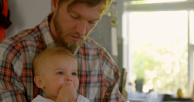 Father with beard holding baby in sunlit kitchen - Download Free Stock Images Pikwizard.com