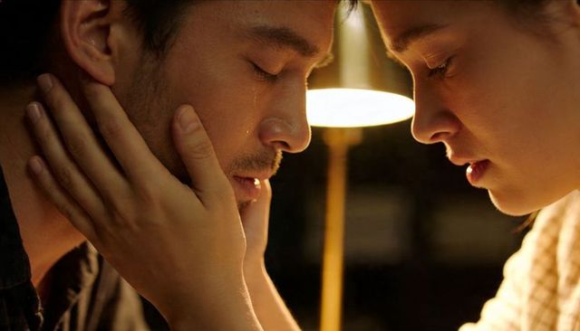 Woman cupping man's face leaning in during emotional moment by warm lamplight