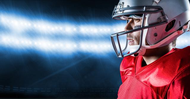 American football player wearing helmet and red jersey standing under stadium lights. Ideal for sports-related promotions, motivation campaigns, event advertising, and athletic gear used in creating motivational posters for sports teams.