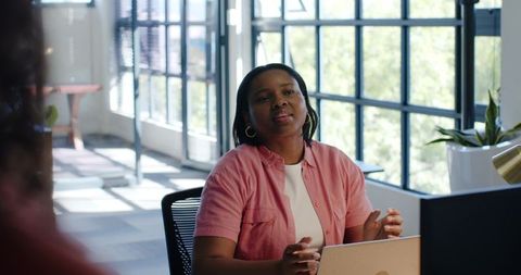 African american professional woman leading office meeting with laptop in sunlit workspace