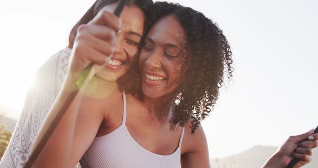 Two women, one Asian and one African American, enjoying a moment while swinging outdoors. They are laughing and look to be having a great time together in a sunlit setting. Perfect for concepts related to friendship, joy, mixed ethnicity, adult bonding, happiness and outdoor activities.