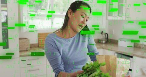 Mid adult woman unpacking groceries and arranging leafy greens in modern kitchen