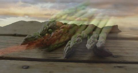 Fresh asparagus spears lying on rustic wood board with coastal sunset double exposure