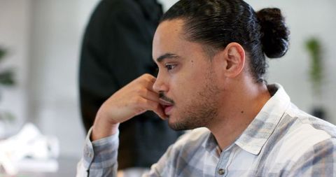 Focused young professional with bun concentrating at computer desk in open office workspace