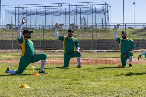 Three baseball players kneeling and raising hands during team warmup on diamond