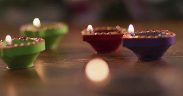 Four lit candles in decorative clay pots on wooden table top, bokeh flame in foreground. diwali festival, celebration, tradition and ceremony concept.