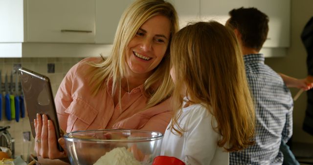 Mother teaching daughter baking at home. Glass bowl with ingredients on counter. Modern, bright kitchen. Ideal for family, cooking recipes, home-life topics.