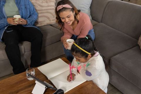 Parents watching daughter drawing in sketchbook at cozy living room coffee table