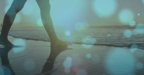 Woman walking barefoot on wet sand at sunset with sun glare bokeh and footprints