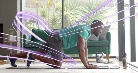 Man performing plank workout at home near large window with kettlebell, teal shirt core strength