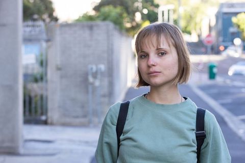 Young woman standing on city street wearing green sweatshirt and backpack, casual portrait