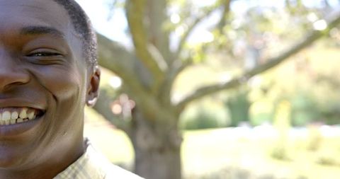 Young African American Man Smiling in Sunny Park with Tree