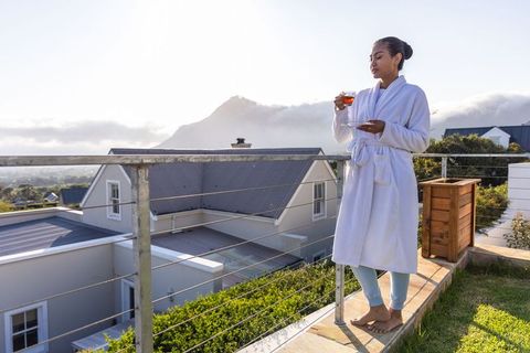 Asian woman enjoying morning tea on balcony in white bathrobe with mountain view at sunrise