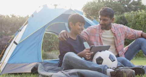 Father and Son Bonding by Camping Tent with Tablet and Soccer Ball