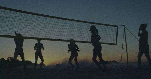 Silhouetted women playing beach volleyball at dusk jumping and spiking against sunset horizon
