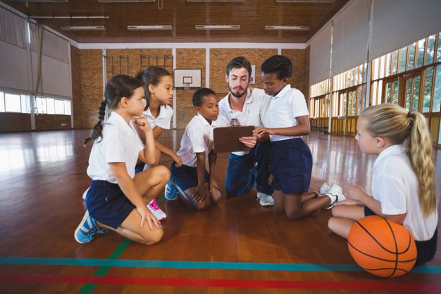 Coach discussing strategy with school kids in a basketball court. Ideal for educational materials, sports training guides, teamwork and leadership concepts, and promoting physical education in schools.