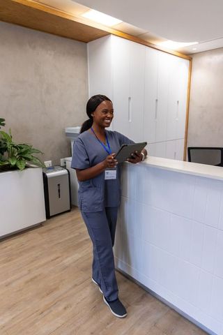 Smiling healthcare professional at clinic reception holding tablet wearing gray scrubs