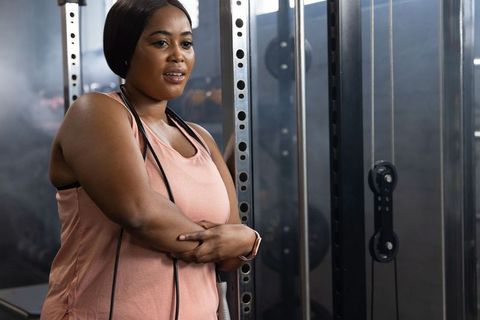 Confident African American Woman Resting by Gym Rack with Jump Rope After Workout Showing Strength