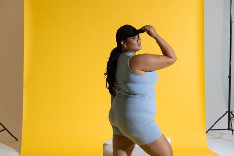 Curvy model posing in ribbed blue athleisure set wearing black cap on yellow backdrop