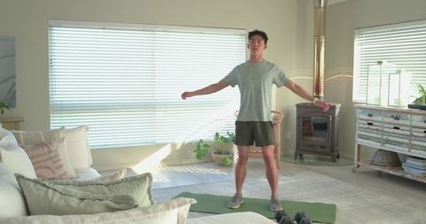 Man doing home workout on green mat with hex dumbbells in sunlit living room