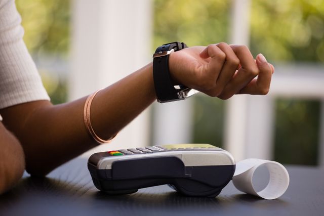 This image shows a woman making a contactless payment using her smartwatch at a card reader in a cafe. Ideal for illustrating modern payment methods, digital transactions, and the convenience of wearable technology in everyday life. Suitable for use in articles, blogs, and advertisements related to fintech, technology, and retail.