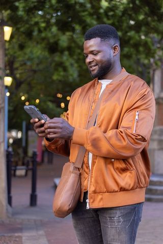 African american man checking smartphone on urban evening plaza in orange jacket