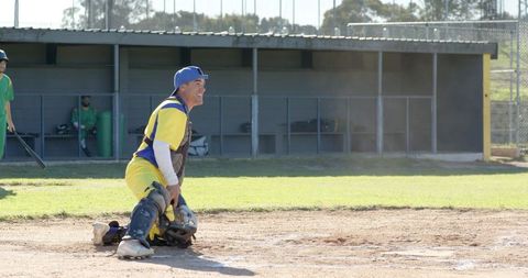 Catcher kneeling at home plate during recreational baseball game, smiling and ready