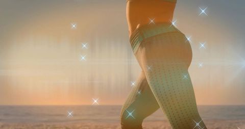 Backlit silhouette of woman in high-waisted leggings on beach at golden hour